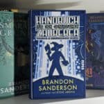 Ein Foto von einem Bücherregal, in dem das Buch Handbuch für den genügsamen Zauberer: Überleben im mittelalterlichen England von Brandon Sanderson steht.